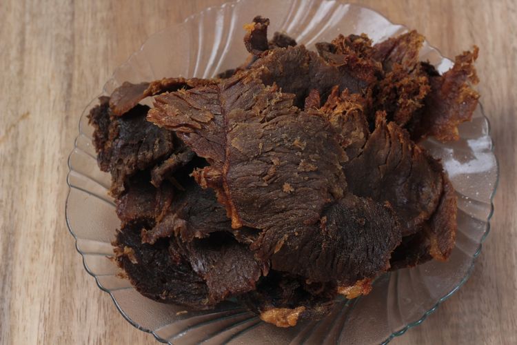 Piring berisi irisan Dengdeng Nabati yang terlihat menyerupai daging asli, disajikan dengan irisan tomat dan selada sebagai garnis